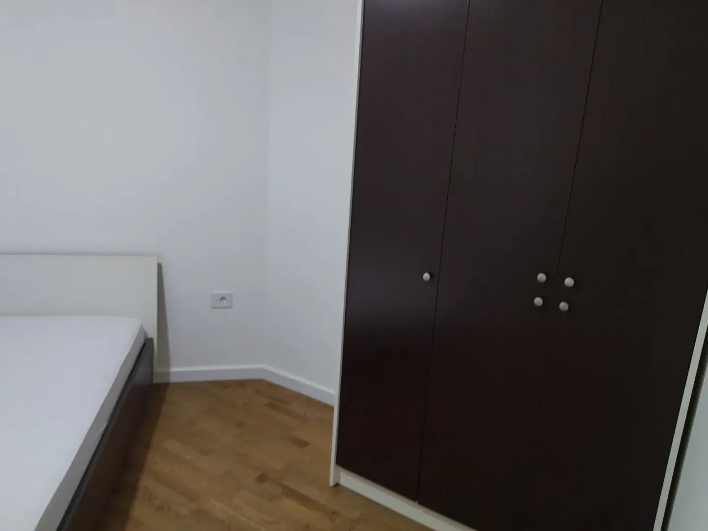 Spavaća soba sa bračnim krevetom i tamnim drvenim ormarom.