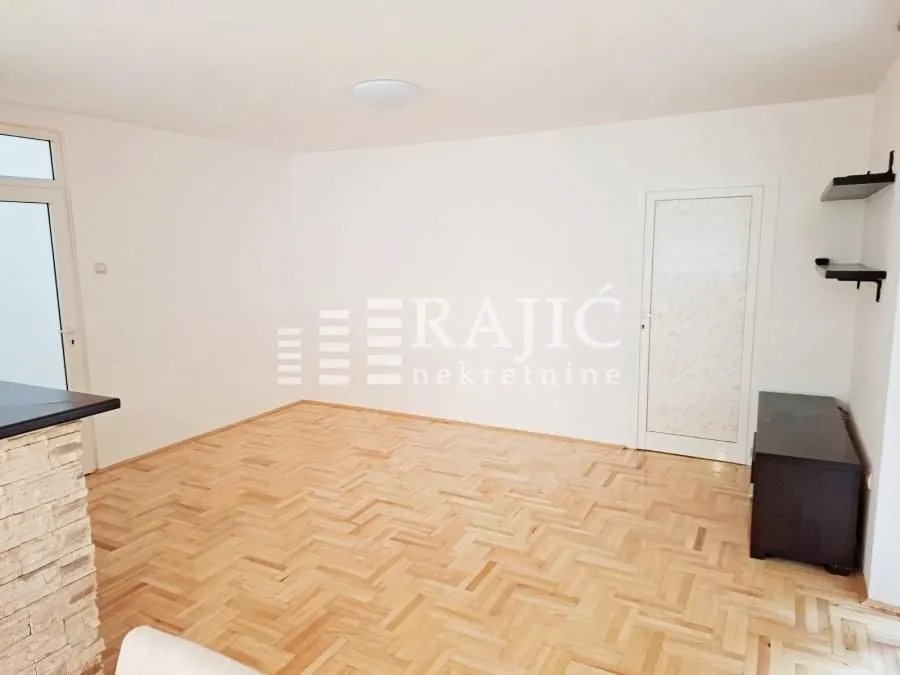 Empty living room with parquet flooring and white walls.