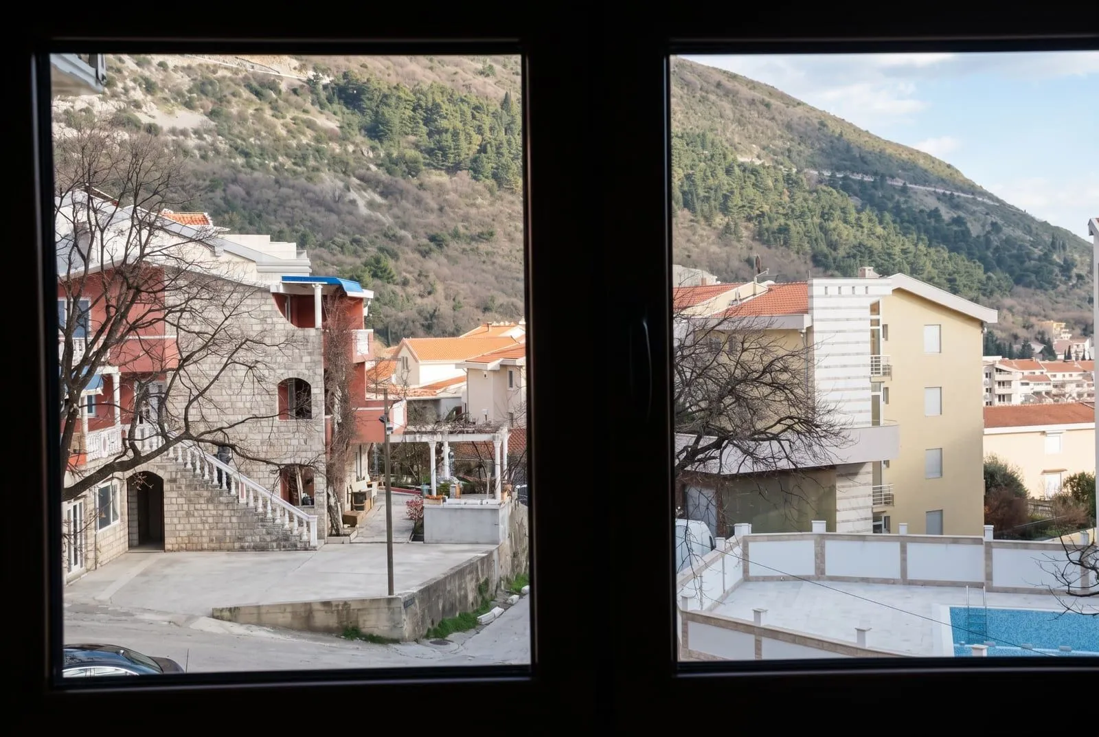 Pogled kroz prozor na okolna brda i susjedne zgrade.