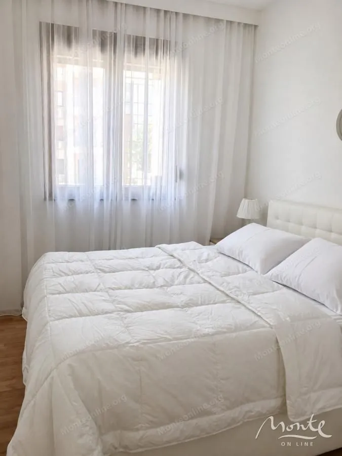 Namještena spavaća soba sa velikim bračnim krevetom i prozorom prekrivenim zavesama.