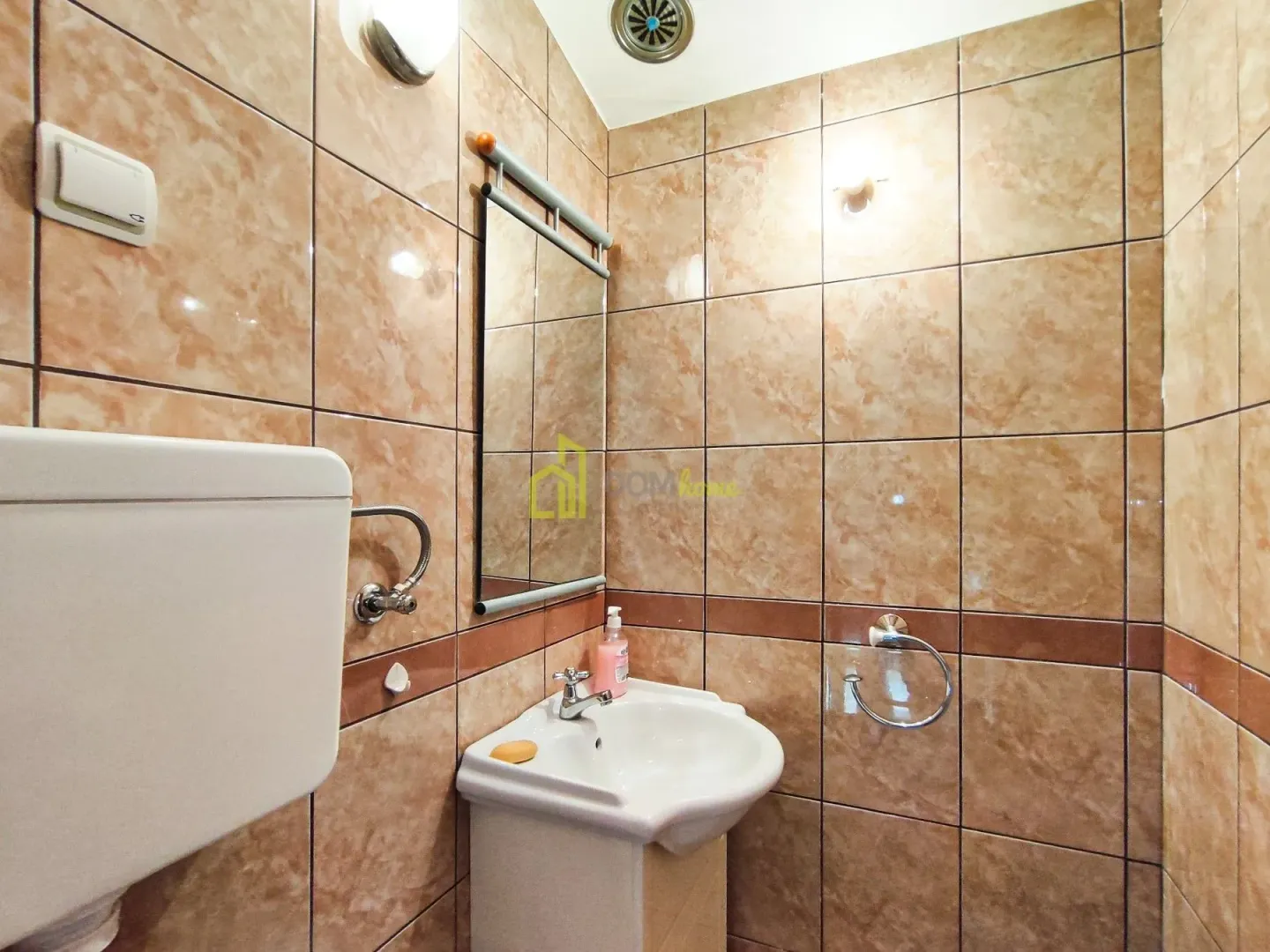 Small bathroom tiled in brown ceramic tiles with a washbasin and a mirror.