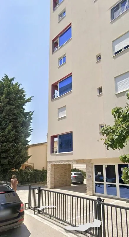 Pogled na spoljašnjost stambene zgrade sa parkingom i ulazom.