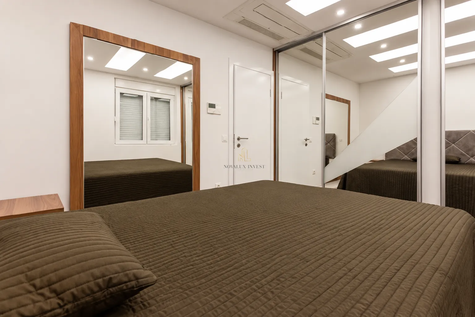 Modern bedroom with a double bed, large mirror, and fitted wardrobe.