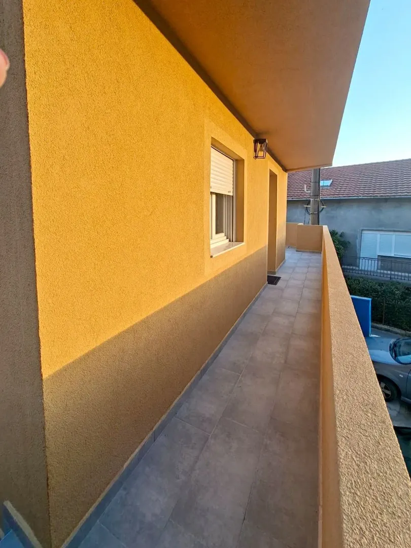 Pogled na dugačak balkon sa popločanim podom i žutom fasadom.
