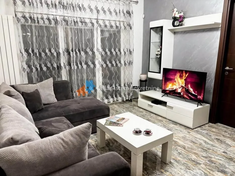 Udobna dnevna soba sa garniturom, TV komodom i velikim prozorom.