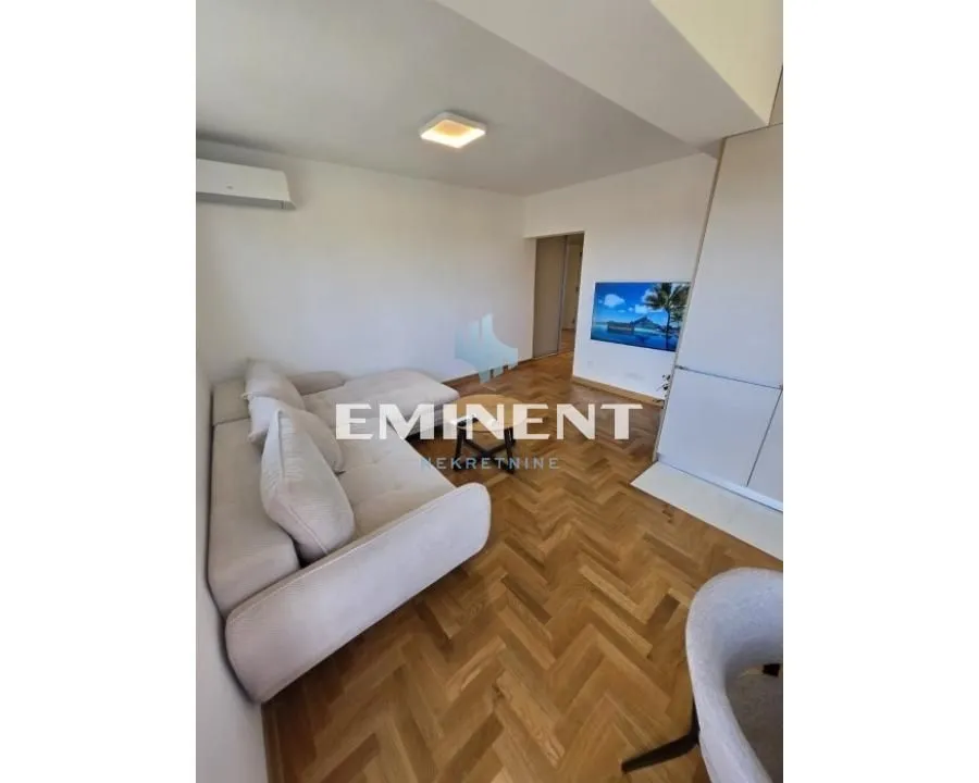 Living room with a corner sofa, television, and parquet flooring.