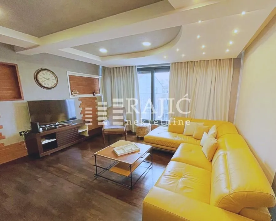 Living room with a yellow sofa, TV, and drop ceiling with lighting.