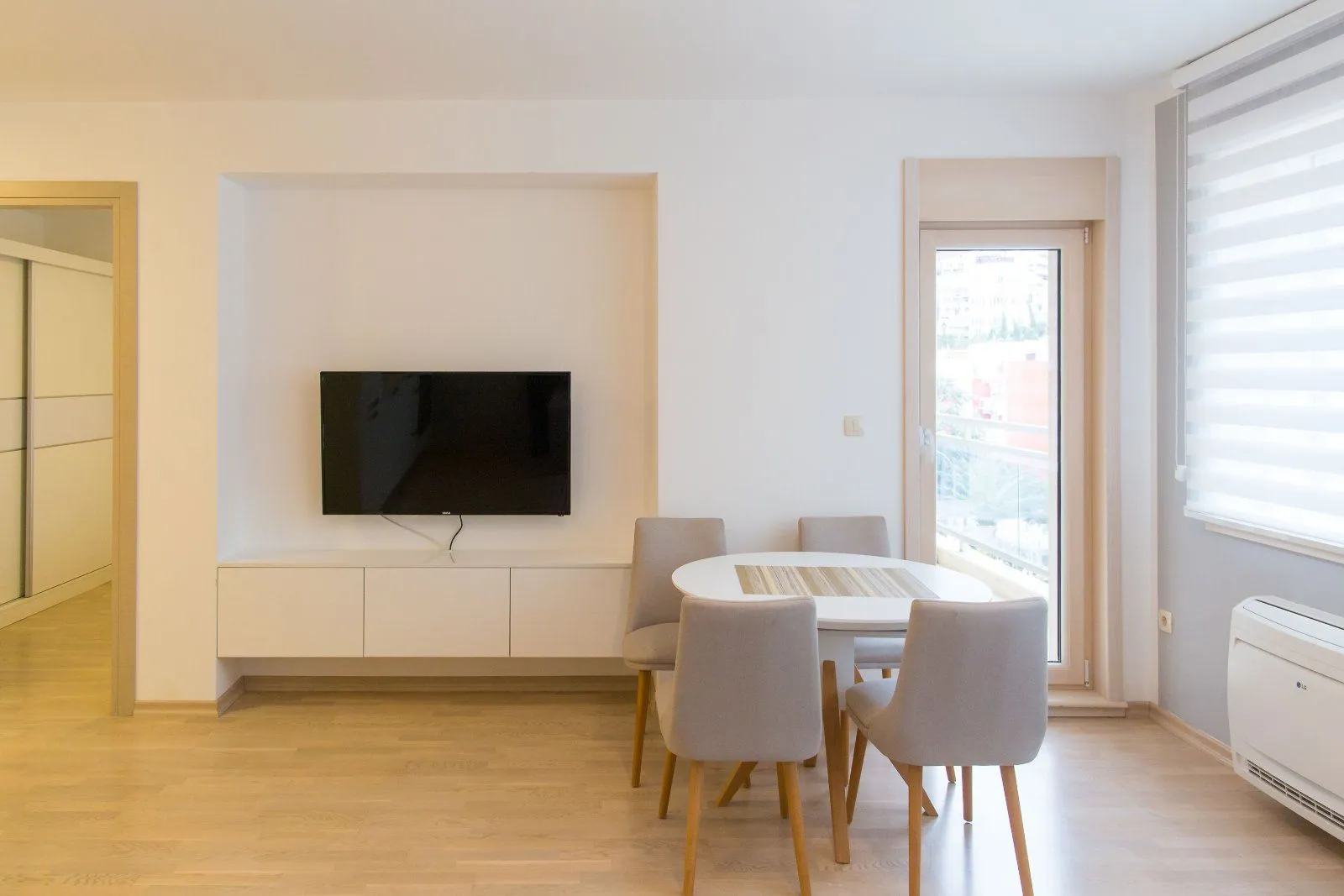 Living room with a dining table and chairs, wall-mounted TV, and access to the terrace.