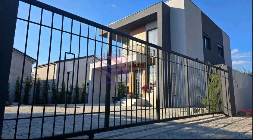 Pogled na dvorište i fasadu kuće sa crnom metalnom kapijom.