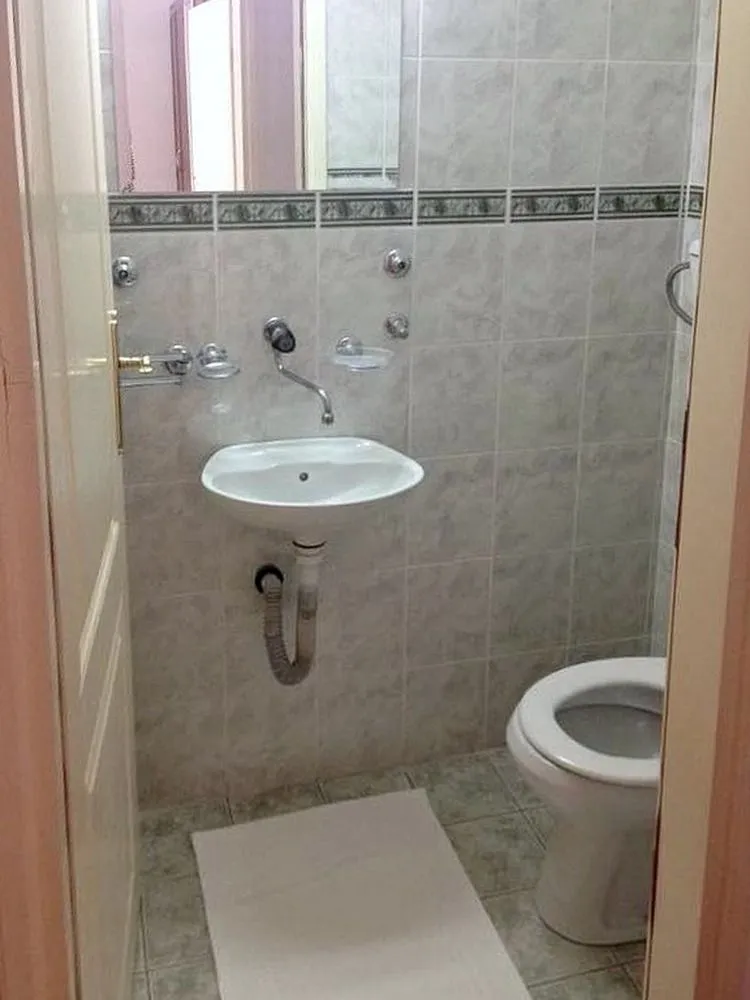 Manje kupatilo obloženo keramičkim pločicama sa umivaonikom i šoljom.