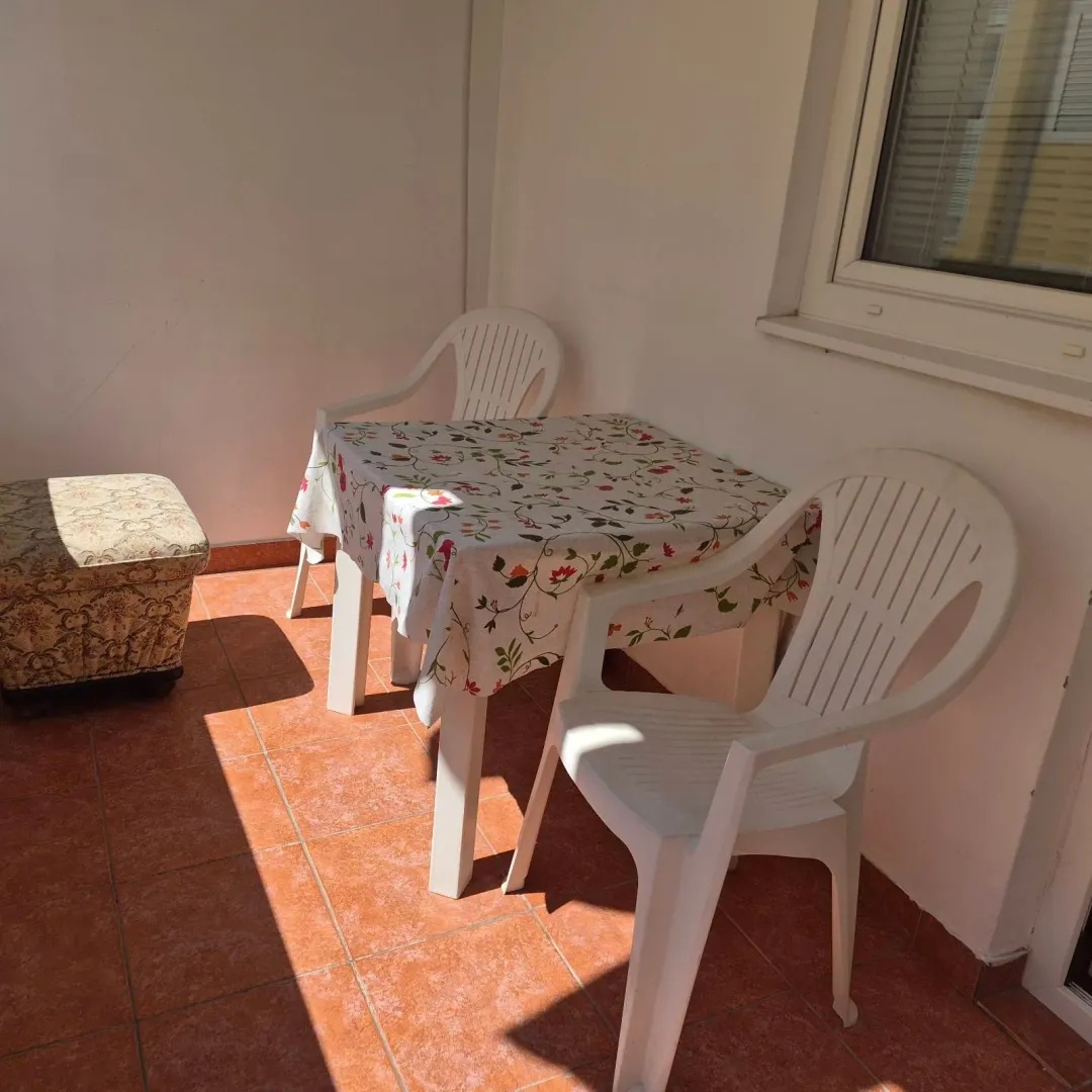 Covered terrace with a table, plastic chairs, and a footstool.