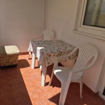 Covered terrace with a table, plastic chairs, and a footstool. - image 10
