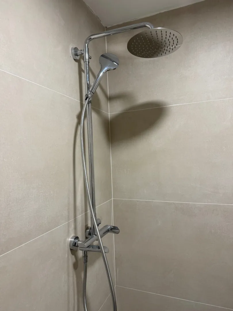 Close-up of a modern shower system in a sand-tiled bathroom.
