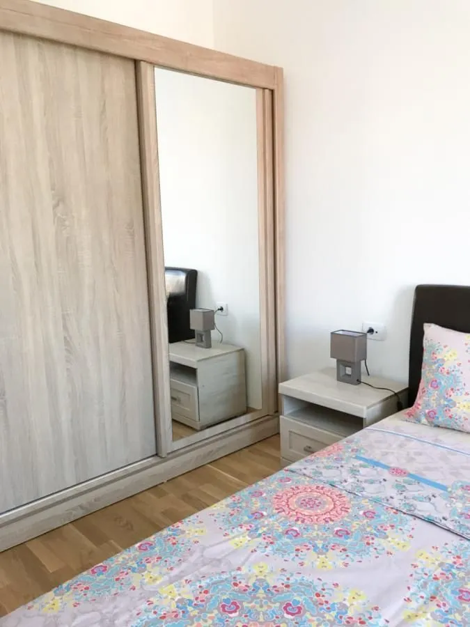Spavaća soba sa velikim garderoberom sa ogledalom, krevetom i noćnim stočićem.
