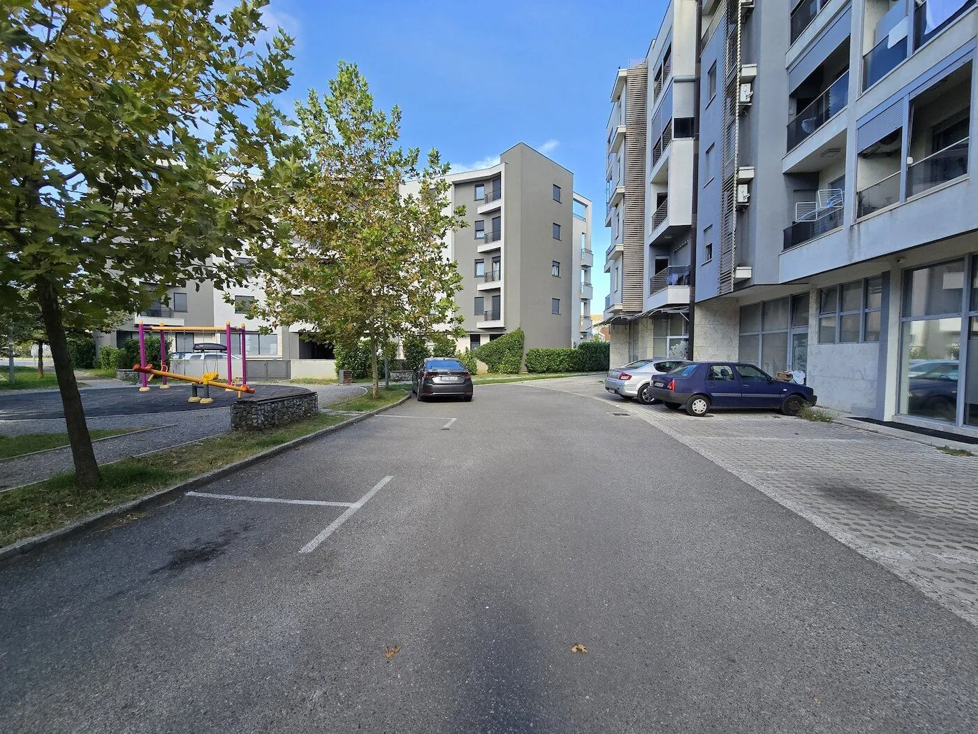 Eksterijer stambene zgrade sa parkingom i igralištem ispred.