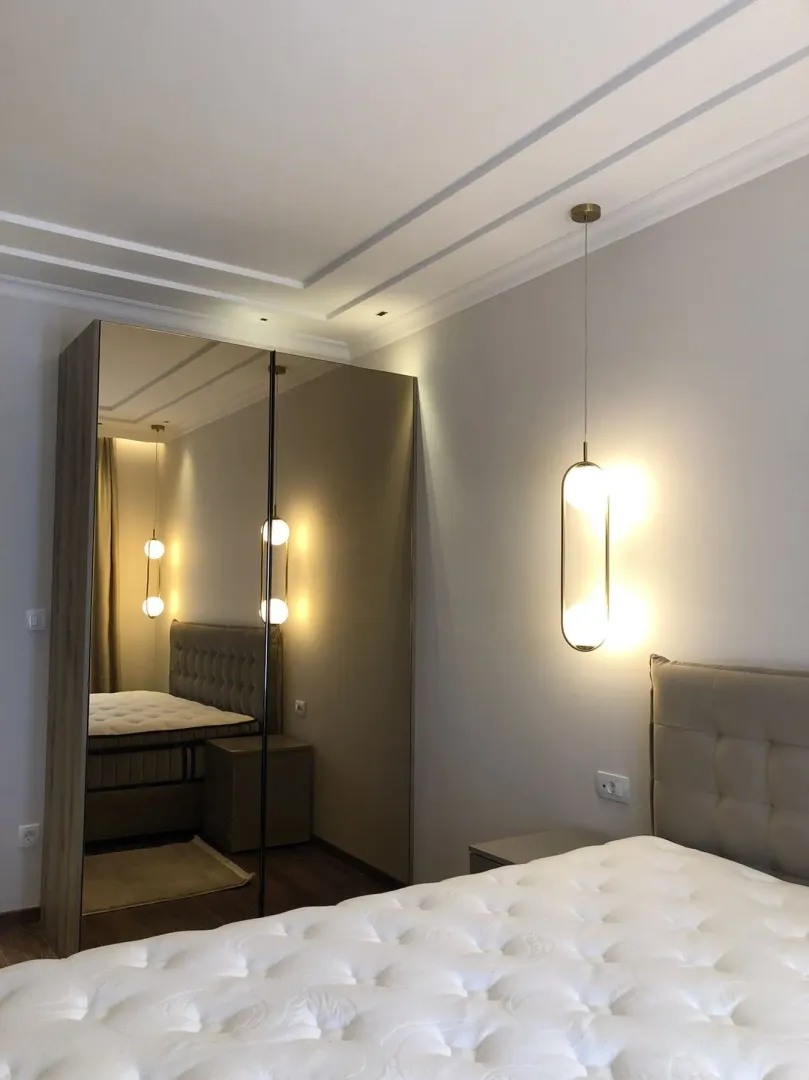 Modern bedroom featuring a large mirrored wardrobe and stylish pendant lighting.