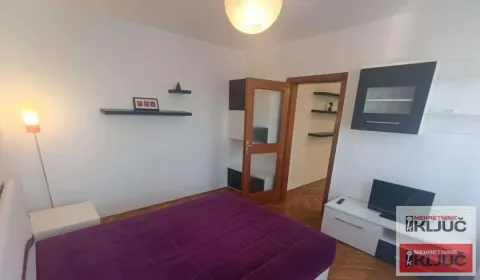 Nameštena spavaća soba sa bračnim krevetom, TV komodom i policama na zidu. - image 4