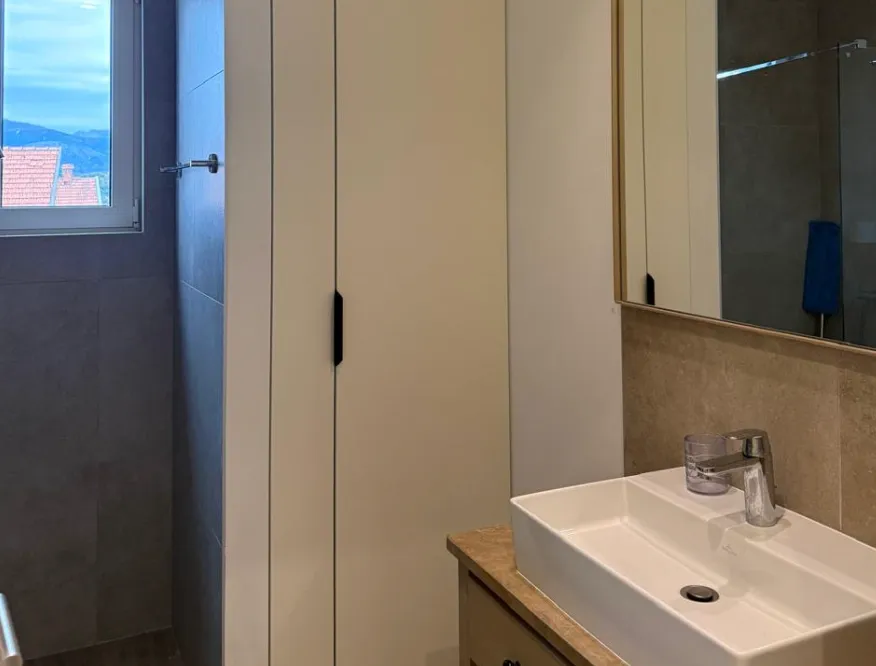 Moderne kupatilo sa umivaonikom, ogledalom i ugradnim ormarićem.