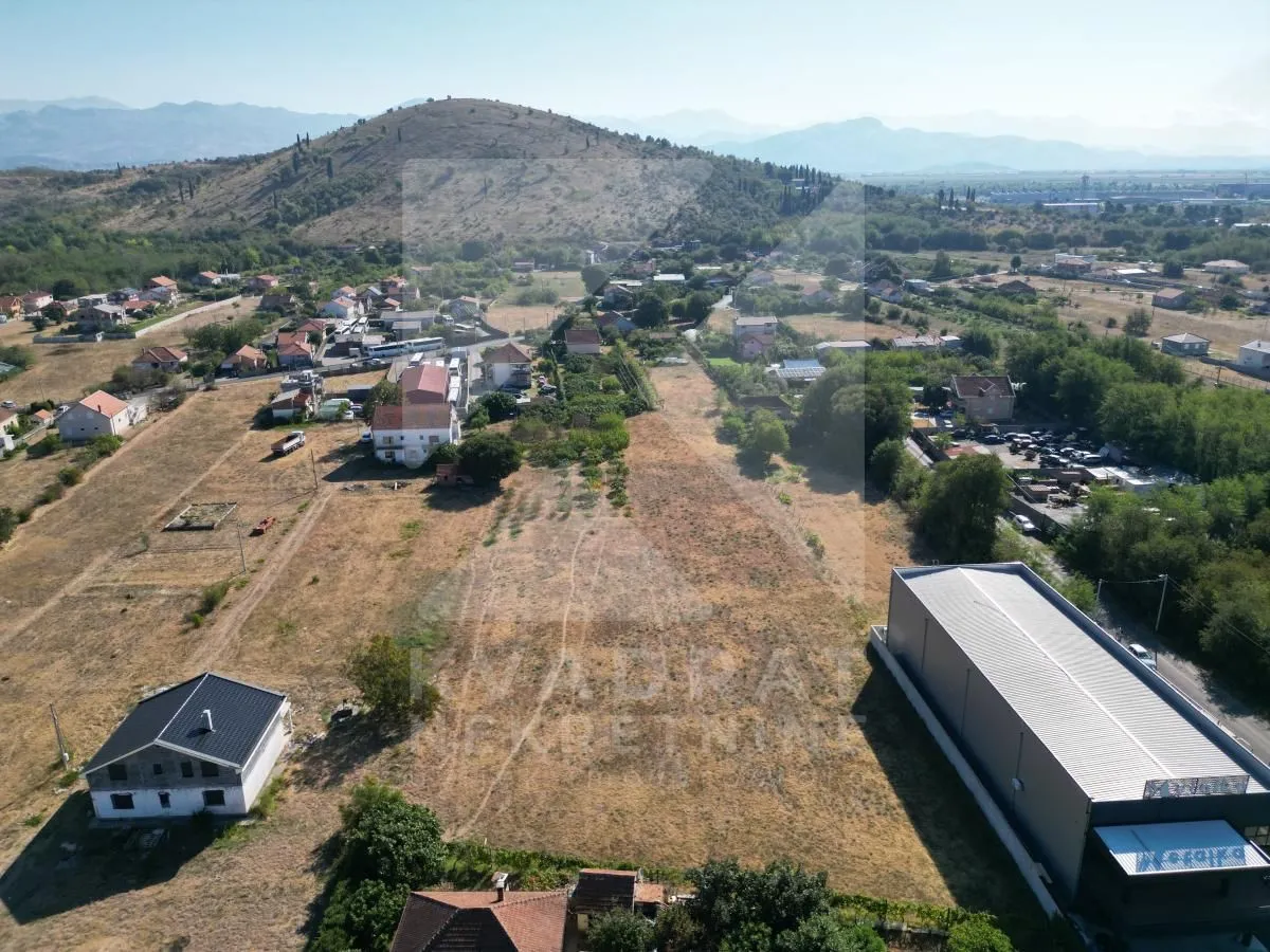 Pogled iz vazduha na zemljište i okolno naselje sa brdom u pozadini.