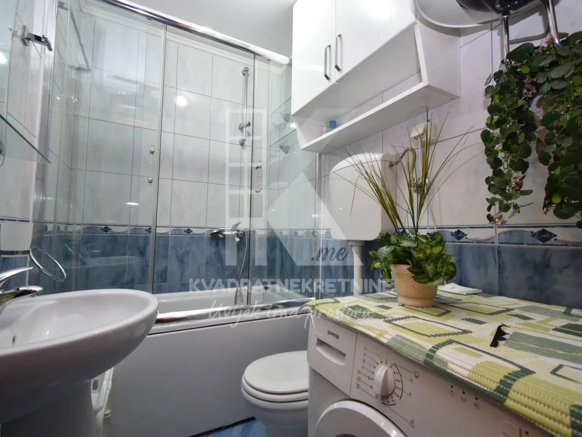 Compact bathroom with bathtub, glass shower screen, washbasin and washing machine.