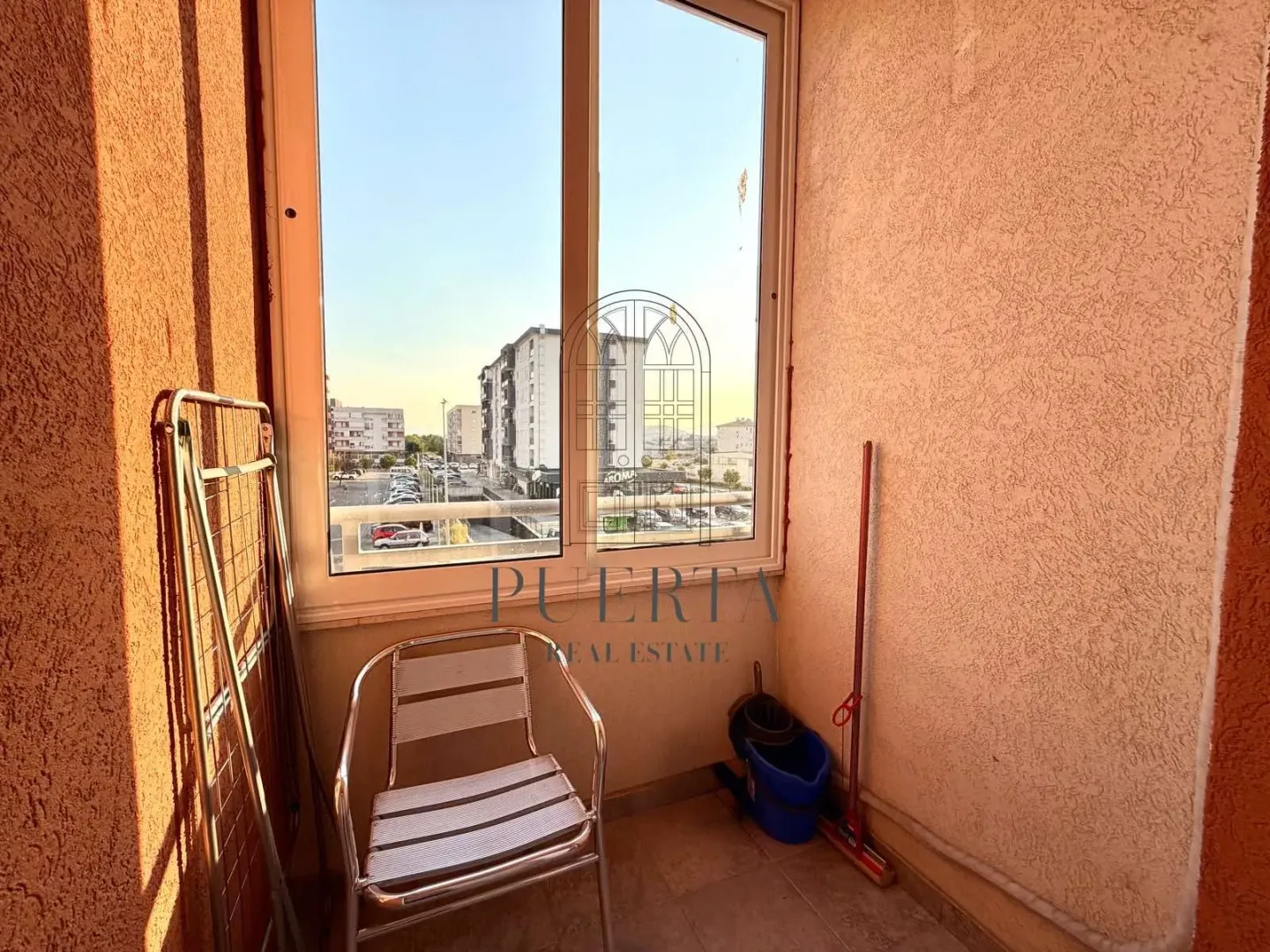 Smaller covered balcony with a chair, drying rack, and city view.