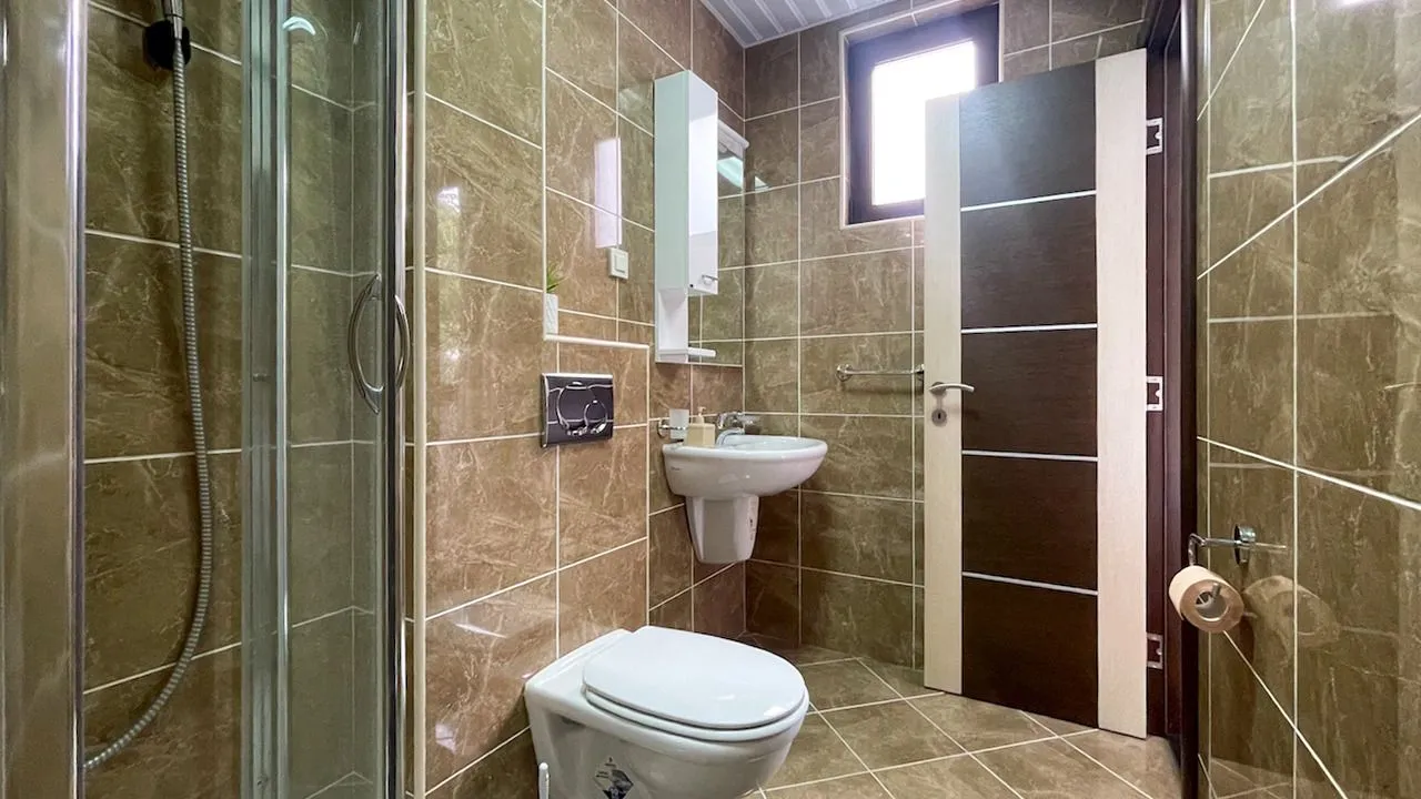 Kupatilo obloženo keramičkim pločicama sa tuš kabinom, umivaonikom i wc šoljom.