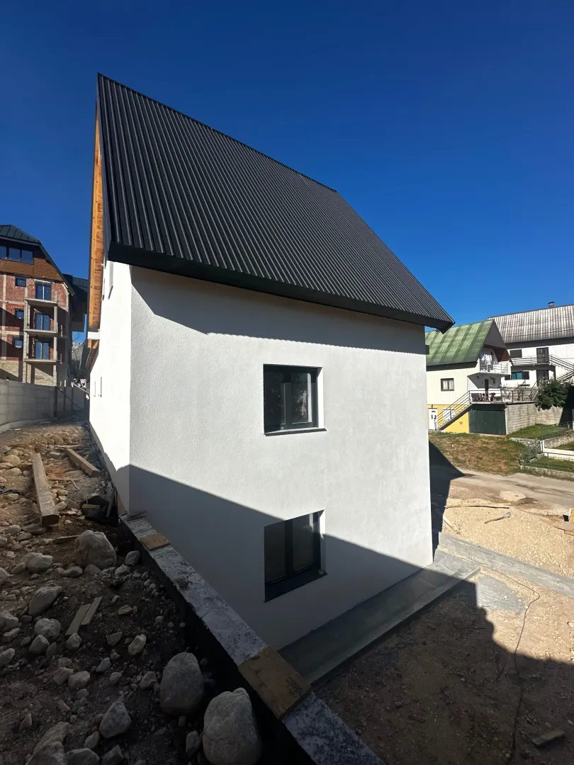 Pogled na spoljašnjost kuće sa bijelom fasadom i tamnim krovom.