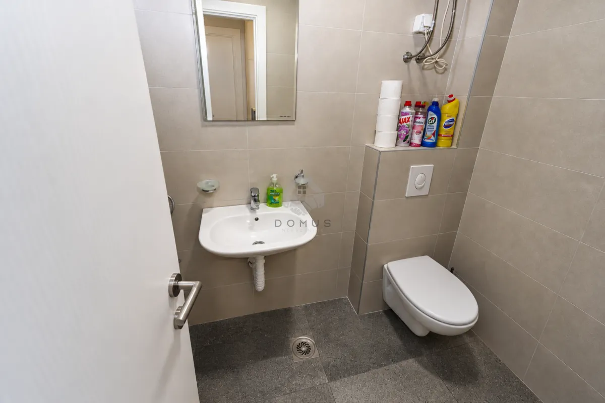 Compact bathroom with a sink, mirror, and toilet tiled with ceramic tiles.