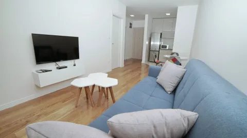 Dnevna soba sa plavom garniturom, TV-om i pogledom na kuhinju u pozadini. - image 2