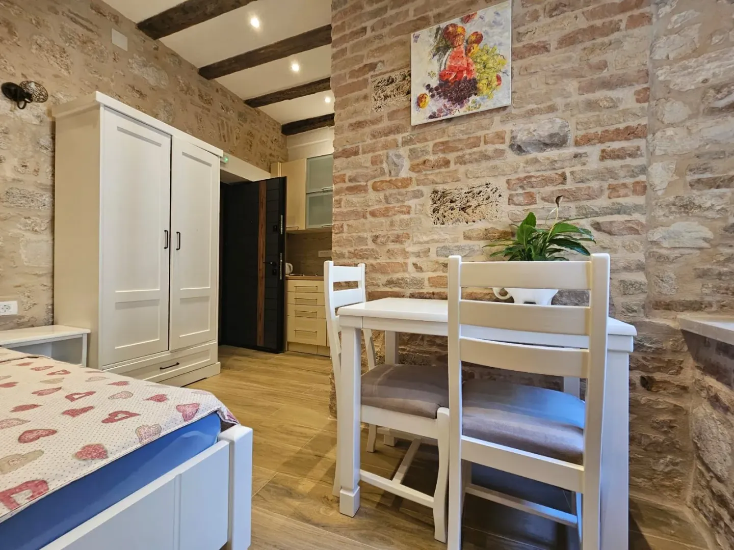 Namještena spavaća soba sa zidom od kamena i bijelim namještajem.