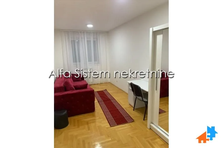 Manja dnevna soba sa crvenom garniturom, radnim stolom i parketom.