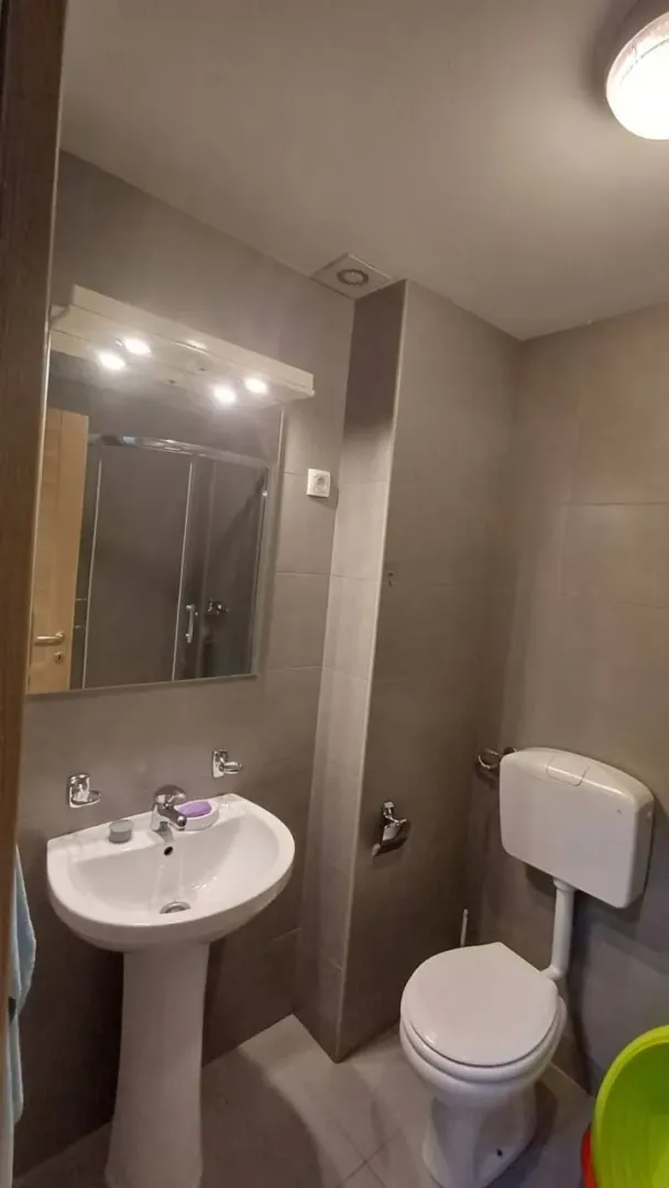 Kupatilo opremljeno umivaonikom, WC šoljom i ogledalom.