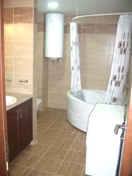 Kupatilo opremljeno umivaonikom, ugaonom kadom, bojlerom i pločicama u braon tonovima. - image 6