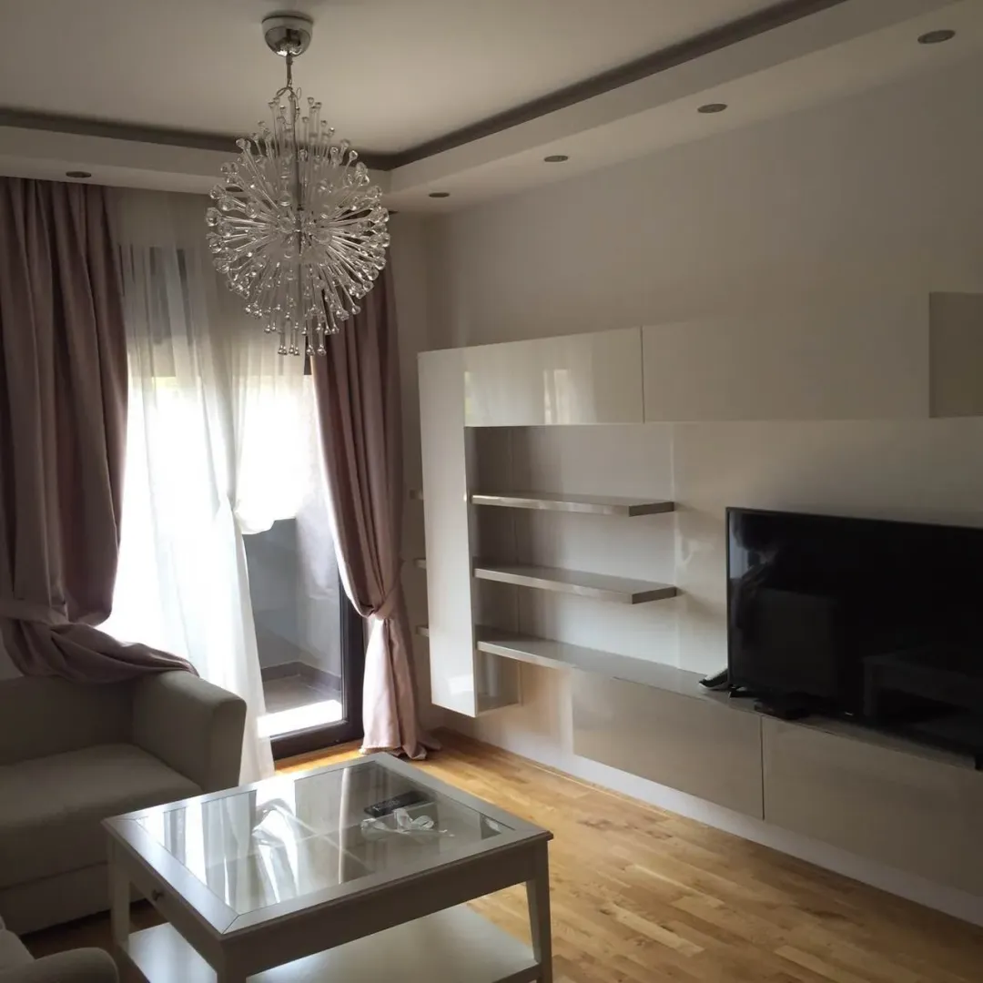 Bright living room with a modern chandelier, TV unit, and glass coffee table.