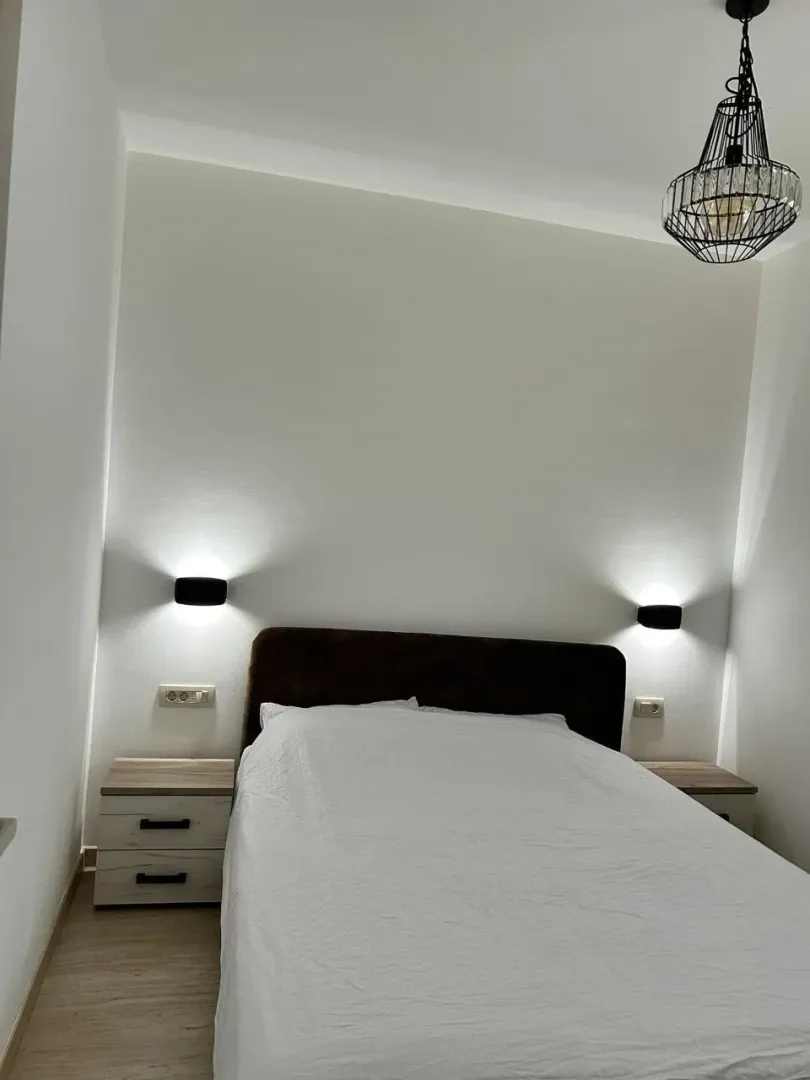 Uređena spavaća soba sa bračnim krevetom, noćnim stočićima i modernom rasvjetom.