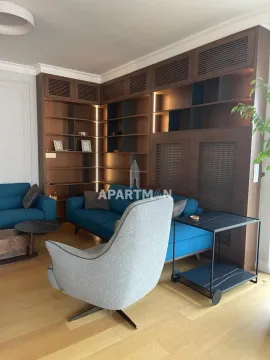 Dnevna soba sa plavim sofama, foteljom i velikim drvenim regalom. - image 6