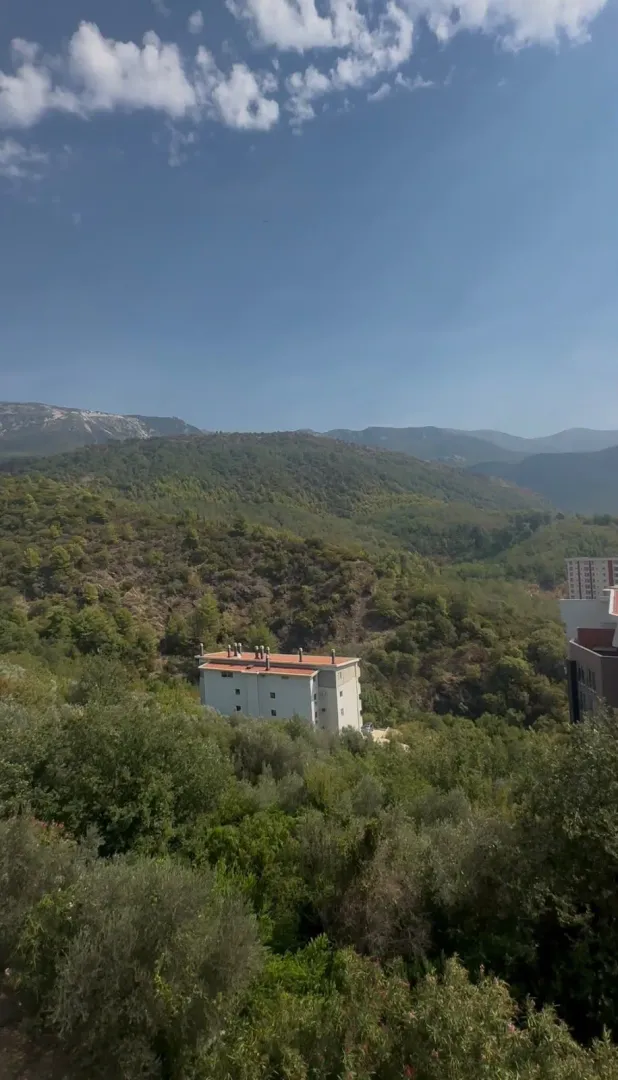 Pogled iz apartmana na šumovite planine i okolne zgrade.