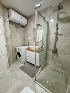 Modern bathroom equipped with a shower cabin, washbasin, and washing machine. - image 15