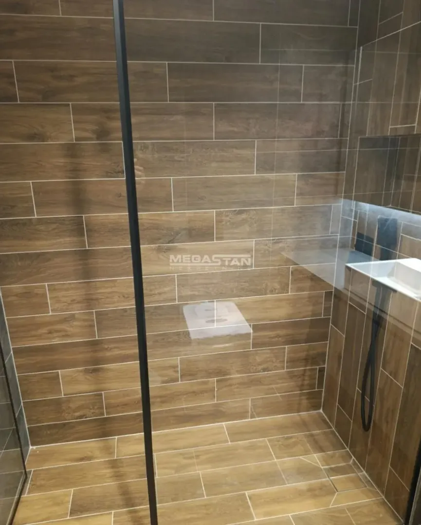 Moderno kupatilo sa tuš kabinom i pločicama u imitaciji drveta.