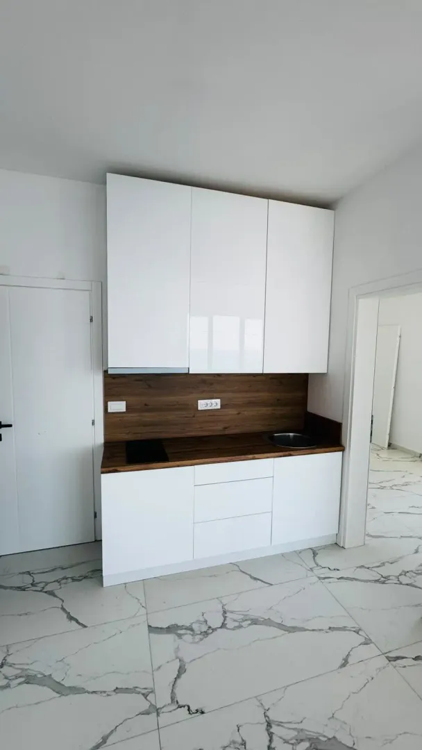 Manja moderna kuhinja sa bijelim elementima i radnom površinom u boji drveta.