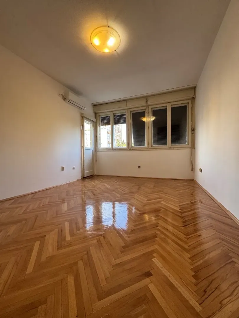 Empty room with parquet flooring and windows.