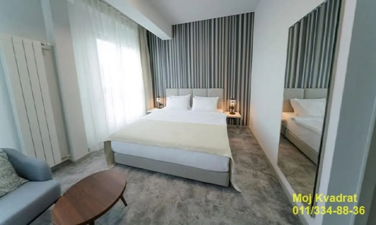 Modern bedroom with a double bed, armchair, and a large mirror.