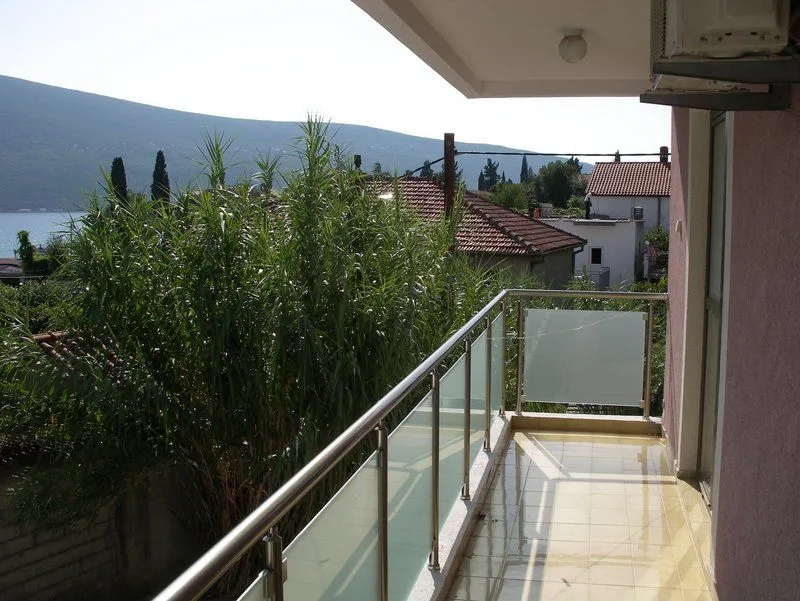 Balkon sa staklenom ogradom i pogledom na more u daljini.
