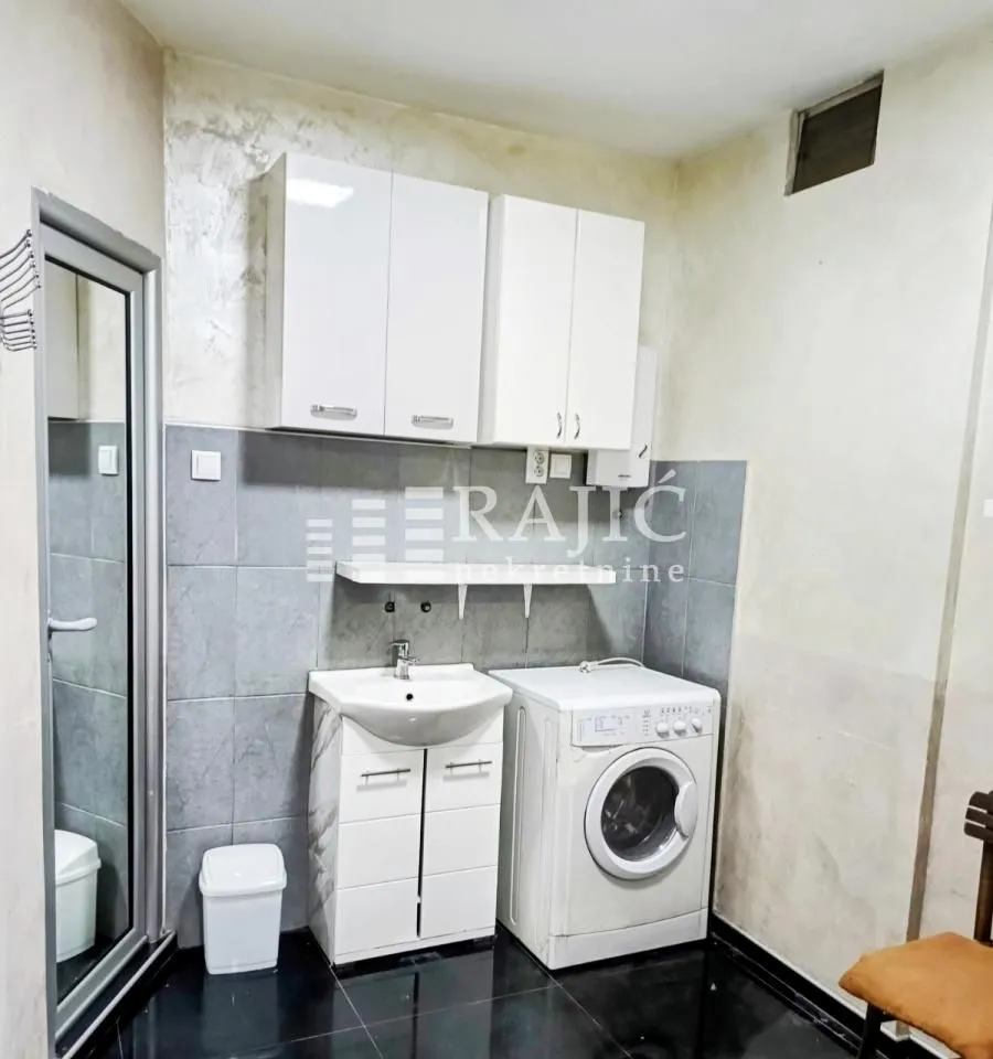 Small bathroom with a sink, white cabinet, washing machine, and upper wall cabinets.