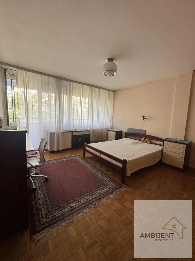 Nameštena spavaća soba sa bračnim krevetom, radnim stolom i izlazom na terasu.