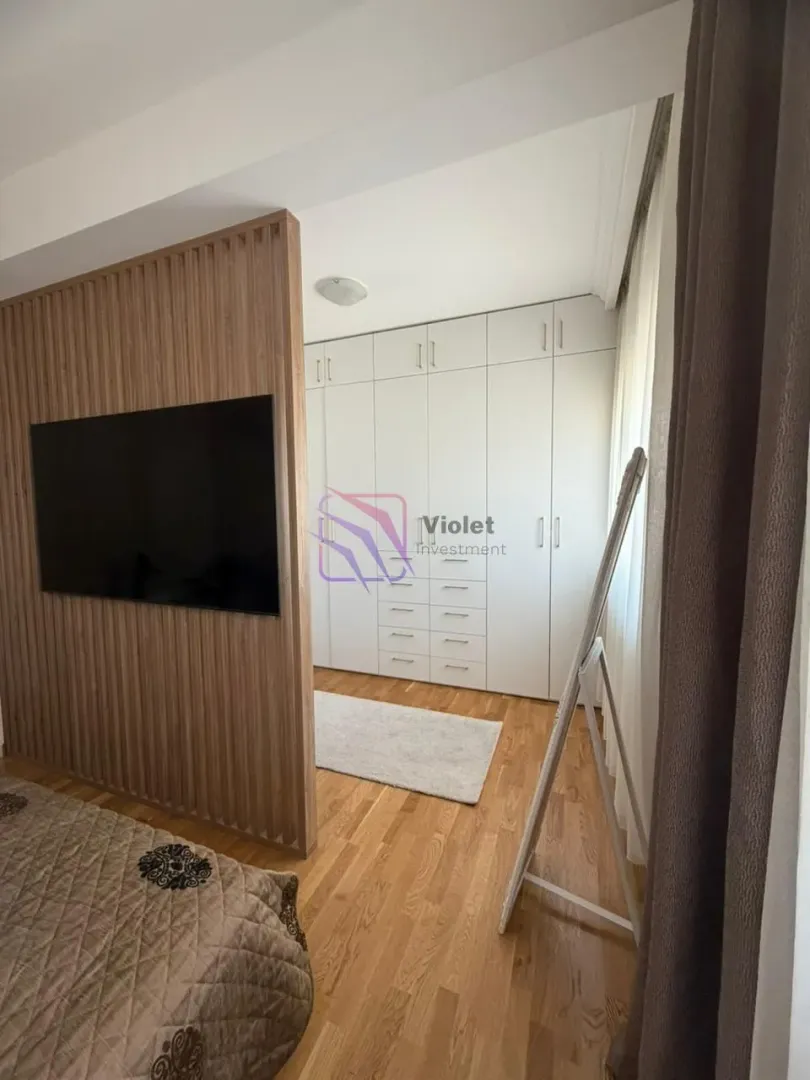 Spavaća soba sa velikim ugradnim garderoberom i drvenom pregradom sa televizorom.