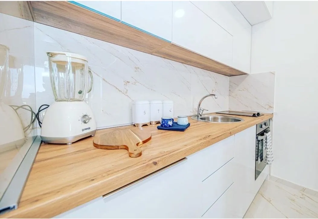 Modern kitchen with white cabinetry, wooden countertop, and built-in appliances.