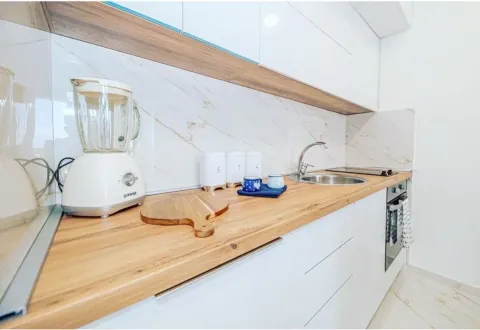Modern kitchen with white cabinetry, wooden countertop, and built-in appliances. - image 4