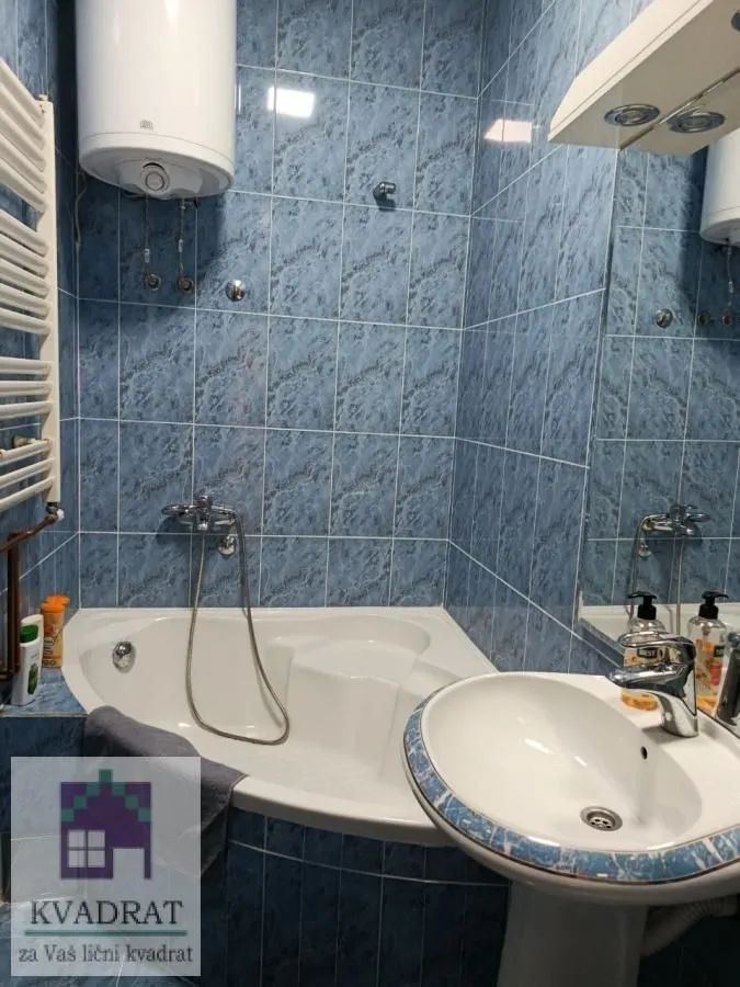 Bathroom equipped with a bathtub, sink, and water heater, tiled throughout.