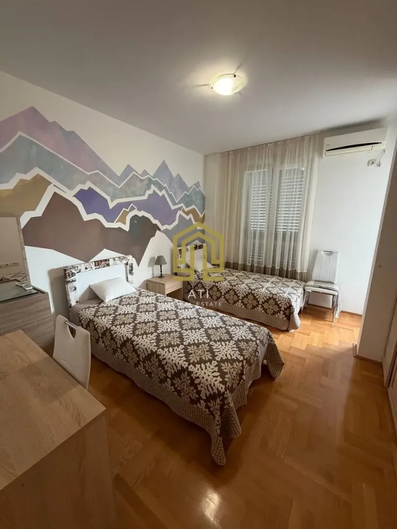 Spavaća soba sa dva kreveta i ukrasnim zidnim motivom.